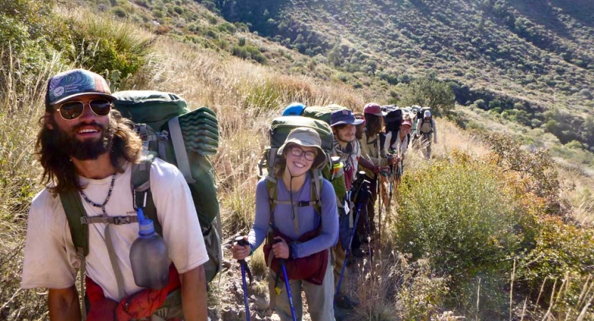 a group of people on a backpacking trip smile at the camera while on trail